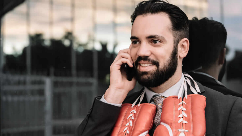 businessman suit talking his mobile phone with red boxing gloves hanging from his neck leaning