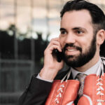 businessman suit talking his mobile phone with red boxing gloves hanging from his neck leaning