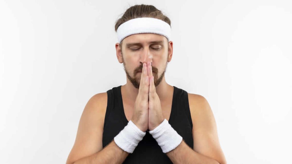 peaceful young handsome sporty man wearing headband wristbands putting hands together pray gesture with closed eyes isolated white space