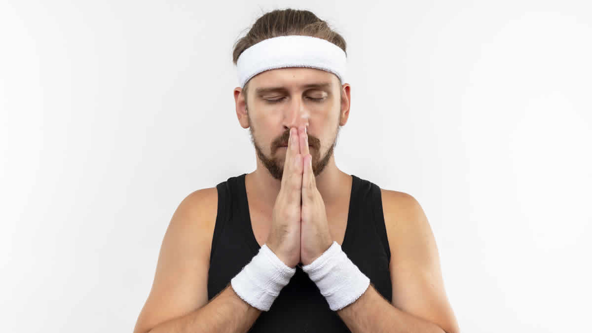 peaceful young handsome sporty man wearing headband wristbands putting hands together pray gesture with closed eyes isolated white space